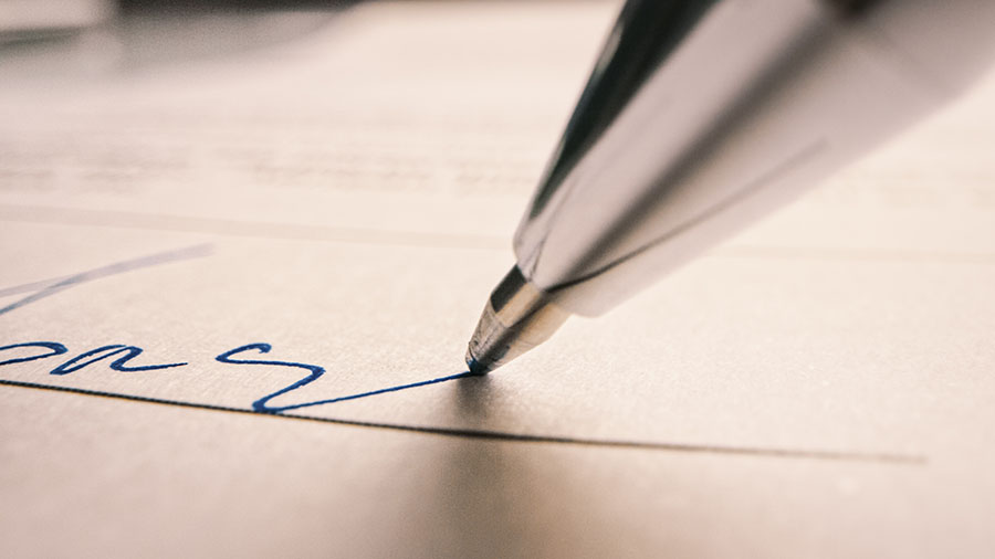 A close up photograph of a pen signing a contract