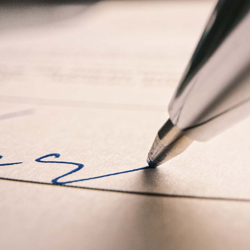 A close up photograph of a pen signing a document